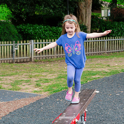 Mädchen balanciert über einen Schwebebalken auf einem Spielplatz.